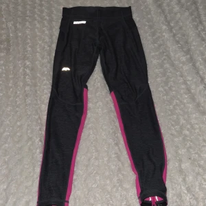 Svarta och rosa träningsleggings från Karhu - Snygga träningsleggings från Karhu i svart med rosa detaljer. De har reflexdetaljer för ökad synlighet och en bekväm passform. Perfekta för löpning eller gymmet!💗💞