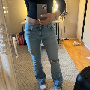 Ljusblå jeans med slitningar - Snygga ljusblå jeans med slitningar på knäna och en bootcut-stil. De har en klassisk femficksdesign och en låg midja. Perfekta för en avslappnad look.