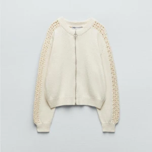 Vit kofta med spetsdetaljer från Zara - Säljer en stilren vit kofta från Zara med unika spetsdetaljer längs ärmarna. Koftan har en dragkedja framtill och ribbade muddar vid ärmslut och nederkant. Perfekt för att lägga till en touch av elegans till din outfit. knappt använd 