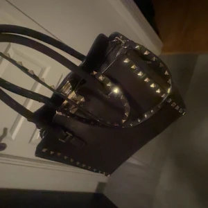 Valentino väska med nitar - Säljer min älskade valentino väska!! Den är i en mörkare brun. Äkta!!!! Påse och kartong med kommer🥰                                                                Man kan göra den mindre om man tar in yttre ”kanterna” som finns på sisita bilden, och använda den lite som man vill💗