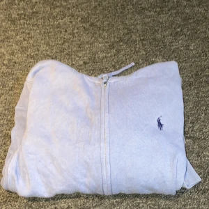Ljusblå hoodie från Ralph Lauren Sport - Säljer en snygg ljusblå hoodie från Ralph Lauren Sport. Den har en dragkedja framtill och en klassisk broderad logga på bröstet. Perfekt för en avslappnad stil. Tillverkad i en mjuk bomullsblandning. OBS! Barnstorlek