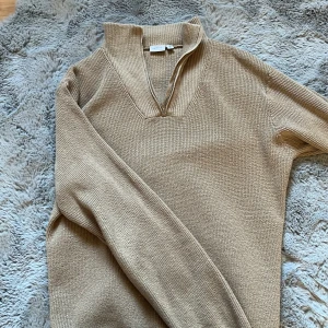 Beige stickad tröja från Name It - Säljer en stilren beige stickad tröja från Name It. Tröjan har en dragkedja vid halsen och långa ärmar, perfekt för kyligare dagar. Den har en klassisk design som passar till många tillfällen.