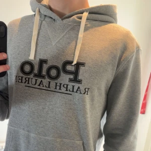 Grå hoodie från Ralph Lauren - Säljer en stilren grå hoodie från Ralph Lauren med klassisk logga på bröstet. Helt nytt skick och knappt använd. Passar M