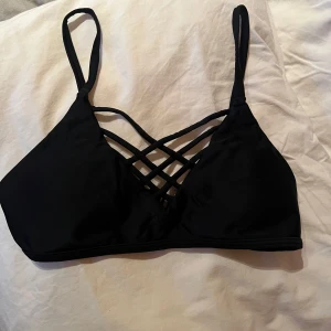 Svart bikiniöverdel  - Snygg svart bikiniöverdel med korsade band framtill. Justerbara axelband och knäppning bak för perfekt passform. På 3e bilden syns det att jag fått fixa fästet till ena axelbandet