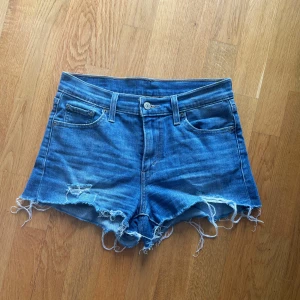 Jeansshorts  - Säljer ett par snygga blå jeansshorts från Levi's med fransiga kanter och klassisk femficksdesign. Storlek w26😊