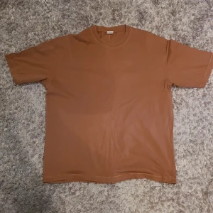 Brun t-shirt från Bershka - Säljer en stilren brun t-shirt från Bershka. Den har en klassisk rund hals och korta ärmar, perfekt för en avslappnad look. Tillverkad i ett mjukt material som känns skönt mot huden.
