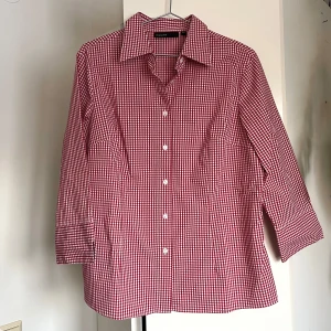 Rutig skjorta  - Figursydd röd-vit rutig skjorta från KappAhl. Skjortan har trekvartsärmar med liten slits och knappar framtill. Använd som oversized och ger hellånga ärmar på mig som har S. Perfekt för en stilren look. Som nyskick.