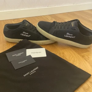 YSL skor - Snygga svarta skor från Saint Laurent med vit logga på sidan och guldtext på plösen. Skorna har en klassisk design med snörning och en vit sula som ger en stilren look. Perfekta för en trendig vardagsstil. Dustbag medföljer skriv gärna om det är någon fråga använda bara några gånger