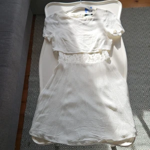 Vit klänning från BikBok - Säljer en söt vit klänning från BikBok med spetsdetaljer i midjan och korta ärmar. Klänningen har en kort längd och en luftig passform, perfekt för varma dagar.