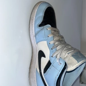 Nike Air Jordans i ljusblått och svart - Snygga Nike Air Jordans i en fräsch ljusblå och svart färgkombination. Skorna har en klassisk design med snörning och den ikoniska Nike-loggan på sidan. Perfekta för att ge din outfit en sportig touch.