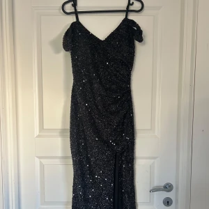 Svart glittrig lång balklänning - Säljer en svart glittrig långklänning med offshoulder-design och smala axelband. Klänningen har en slits framtill som ger en extra touch av glamour. Den har även fodring vid brösten och är lite lång för mig som är 162 cm☺️