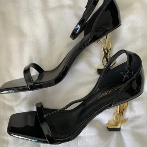 Svarta klackskor från Saint Laurent - Snygga svarta klackskor från Saint Laurent med en unik guldklack i form av YSL-loggan. Skorna har en elegant remdesign och är perfekta för att ge en lyxig touch till din outfit. Pris kan diskuterast!
