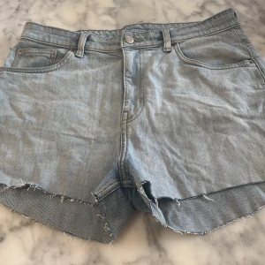 Ljusblå jeansshorts med fransar - Snygga ljusblå oversized jeansshorts med fransiga kanter och klassisk femficksdesign. Perfekta för en avslappnad sommarlook. De har en knapp och dragkedja framtill samt bälteshällor.