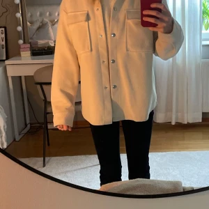 Beige vårjacka med knappar - Säljer en stilren beige kappa med knappar framtill och två stora bröstfickor. Perfekt för alla outfits och jackan är knappt använd.