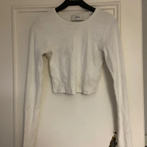 Vit ribbad tröja från JJXX - Säljer en stilren vit ribbad tröja från JJXX. Tröjan är croppad med långa ärmar och har en enkel design som passar perfekt till olika outfits. Perfekt för dig som gillar en minimalistisk stil.