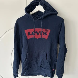 Mörkblå hoodie från Levi's - Säljer en snygg mörkblå hoodie från Levi's med det klassiska röda logotyptrycket på bröstet. Tröjan har en praktisk magficka och justerbar huva med dragsko. Perfekt för en avslappnad stil.