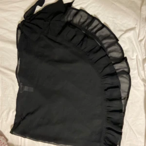 Svart omlottkjol med volang - Snygg svart omlottkjol från Cubus med volangdetaljer. Kjolen är i ett lätt och luftigt material, perfekt för varma dagar. Den har en knytning i midjan för justerbar passform.