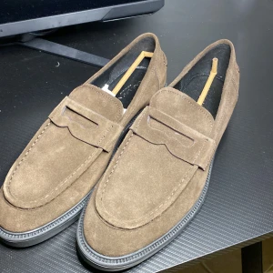 Bruna mockaloafers från Vagabond - Snygga bruna loafers i mocka från Vagabond. Perfekta för en stilren look med en bekväm passform. Skorna har en klassisk design med en robust sula.
