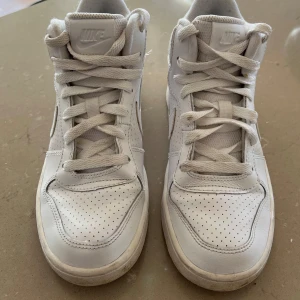 Vita sneakers från Nike - Säljer ett par vita höga sneakers stl 36 från Nike med snörning. Skorna har en perforerad design för extra ventilation och en klassisk Nike-logga på sidan. Perfekta för en stilren look. De är i fint skick och knappt använda (men vita).   Finns att hämta i Sundbyberg alt skickas mot frakt.  Fynda vårskor för endast 300 kr. 