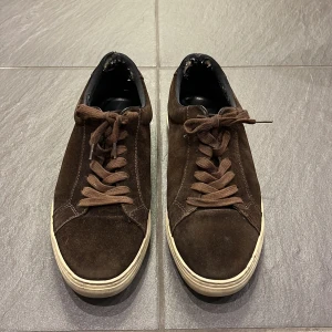 Bruna mockasneakers från Vagabond - Snygga bruna sneakers i mocka från Vagabond med snörning och vit sula. Perfekta för en avslappnad stil. De har en klassisk design med rund tå och är lätta att matcha med olika outfits.