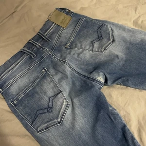  Replay Anbass Jeans - Snygga blå jeans från Replay i modellen Anbass. De har en klassisk femficksdesign och en bekväm passform. Perfekta för en avslappnad stil med en modern touch. W 30 L29