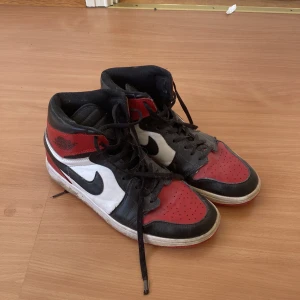 Nike Air Jordans i rött, svart och vitt - Säljer ett par klassiska Nike Air Jordans i rött, svart och vitt. Skorna har hög snörning och den ikoniska Nike-loggan på sidan. Perfekta för dig som älskar sneakers med stil och komfort.