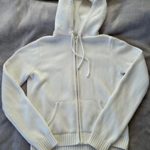 Vit hoodie från Brandy Melville - Säljer en stilren vit hoodie från Brandy Melville. Den är stickad med dragkedja och har en praktisk huva med knytband. Perfekt för en avslappnad look. Fint skick! One size men skulle säga runt storlek S❤️