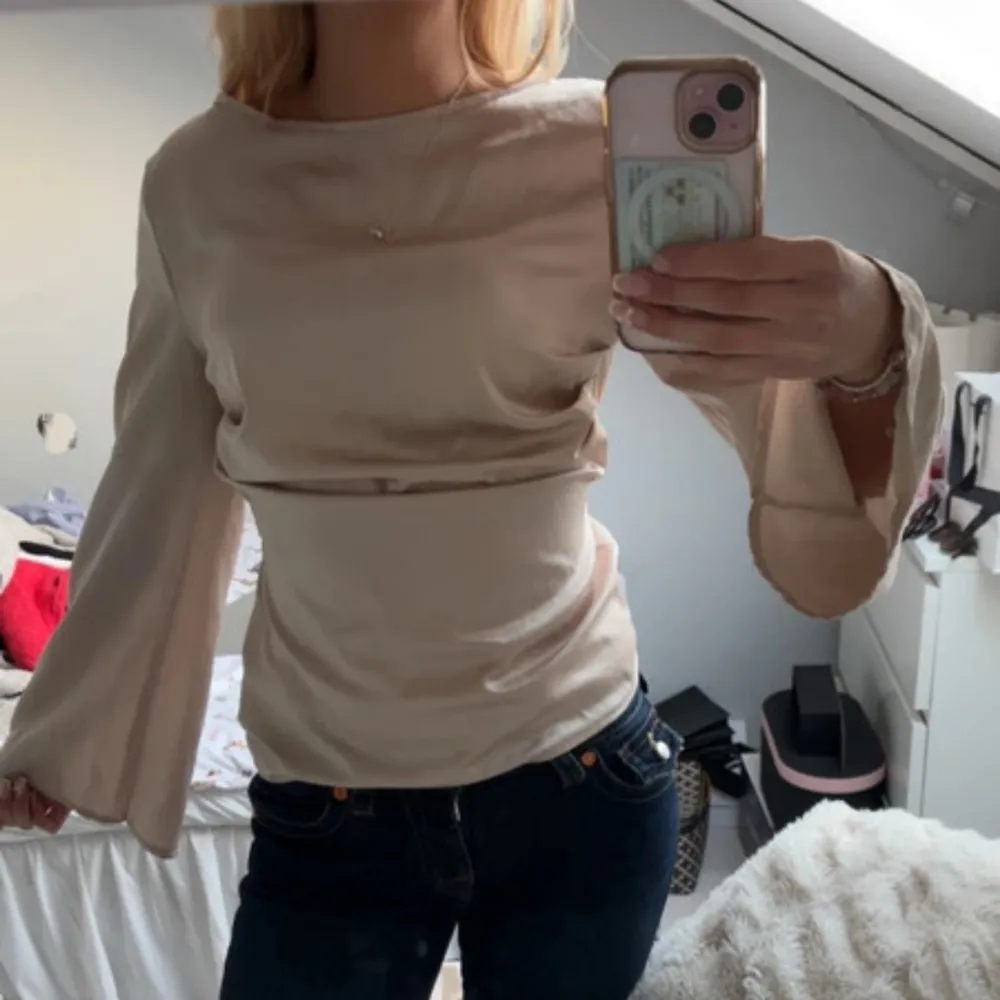 Säljer en stilren beige topp med långa ärmar och en elegant drapering framtill. Perfekt för en chic och avslappnad look. Passar bra till både jeans och kjol.. Puserot.