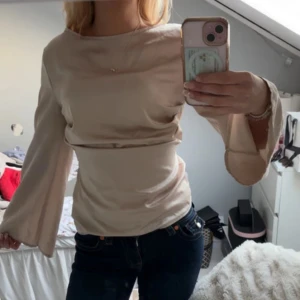 Beige långärmad topp - Säljer en stilren beige topp med långa ärmar och en elegant drapering framtill. Perfekt för en chic och avslappnad look. Passar bra till både jeans och kjol.
