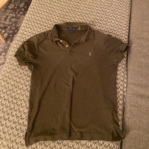 Olivgrön pikétröja från Ralph Lauren - Säljer en stilren olivgrön pikétröja från Ralph Lauren med klassisk krage och knappar. Tröjan har korta ärmar och en liten broderad logotyp på bröstet. Perfekt för en avslappnad men ändå snygg look.