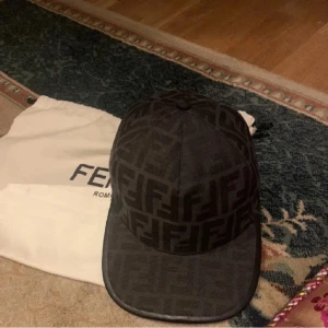 Svart keps från Fendi med monogram - Snygg svart keps från Fendi med deras klassiska FF-monogram över hela kepsen. Kepsen har böjd skärm och är tillverkad i bomull. Perfekt accessoar för att lyfta din outfit.