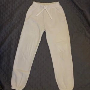 Vita mjukisbyxor från H&M - Säljer ett par vita mjukisbyxor från H&M med resår i midjan och dragsko. Byxorna har även resår vid bensluten och är tillverkade i mjukt material, perfekta för en avslappnad stil.