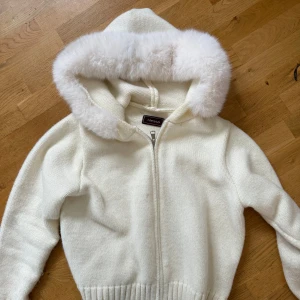 Vit stickad Alessa jacka - Mysig vit stickad jacka från Alessa med dragkedja och stor huva kantad med fluffig riktig päls. Jackan har ribbade muddar och en croppad passform. Fick hem den för 5 dagar sedan och använt den 2-3 gånger och nu har jag insett att det ej är min stil. Nypris 1800kr mitt pris 1000kr.