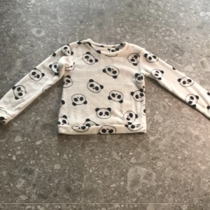 Vit fleece-tröja med pandamönster från Censored - Supermjuk och mysig vit fleece-tröja från Censored med sött svart pandamönster över hela tröjan. Perfekt för att hålla sig varm och bekväm. Långärmad och med rund halsringning.