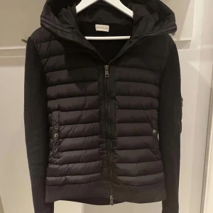 Svart jacka från Moncler - Snygg svart jacka från Moncler med quiltad framsida och stickade ärmar. NFC scan funkar på loggan, storlek XL men eftersom moncler är små i storlek så är de rekommenderat att ta en storlek större, , pris går o diskutera, vid frågor hör av er!