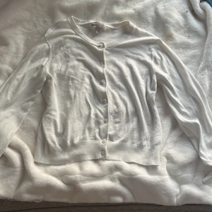 Vit kofta från H&M - Säljer en klassisk vit kofta från H&M med rund halsringning och knäppning framtill. Tröjan har långa ärmar och är tillverkad i ett mjukt, tunt material som passar perfekt till sommaren. 