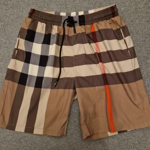  Burberry shorts - Snygga badshorts från Burberry med klassiskt rutigt mönster i beige, brun och svart med en orange detalj. Shortsen passar perfekt till dig som vill ha en fet outfit. Dessa är en av de trendigaste nu. IN OCH KÖP