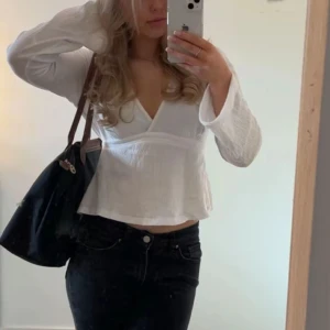 Vit omlottopp med v-ringning - Säljer en vit omlottopp med djup v-ringning och långa ärmar. Toppen har en lätt strukturerad yta och sitter bekvämt med en något lös passform. Perfekt att styla med jeans eller kjol.