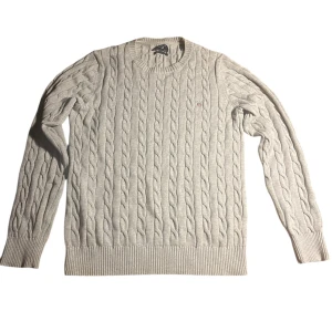 Beige kabelstickad crewneck tröja från Gant - Säljer en klassisk beige kabelstickad tröja från Gant med rund halsringning. Tröjan har långa ärmar och ribbade muddar vid ärmslut och nederkant. Perfekt för lager-på-lager under kyliga dagar.
