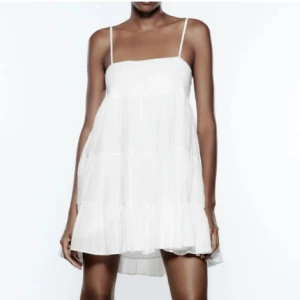 Vit kortklänning med tunna axelband - Supersöt vit kortklänning med tunna axelband och luftig, volangig kjol. Perfekt för varma dagar och ger en lätt och somrig känsla. Klänningen har en lös passform och är tillverkad i ett tunt, flowy material.