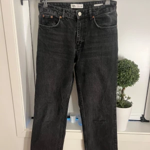 Svarta raka jeans från Zara - Säljer ett par svarta jeans från Zara med raka ben och klassisk femficksdesign. Jeansen har midwaist och silverfärgade knappar. Perfekta för en stilren och avslappnad look.