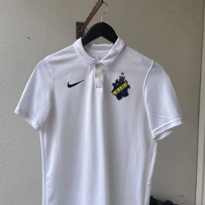 Vit AIK Pike från Nike - Säljer en vit AIK fotbollströja från Nike med klubbmärke på bröstet och Dri-Fit material. Detaljer i gult och svart vid kragen. använd få gånger.