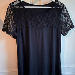 Svart blus med spetsdetaljer från Body Flirt - Säljer en elegant svart blus från Body Flirt med spetsdetaljer på ärmarna och överdelen. Blusen har korta ärmar och en rund halsringning. Perfekt för en stilren look.