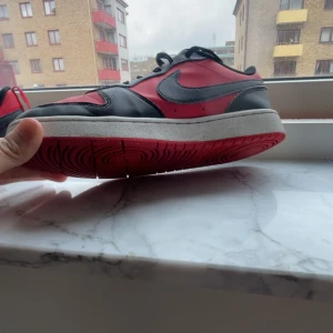 Nike sneakers i rött och svart Nike skor - Snygga Nike sneakers i en klassisk röd och svart färgkombination. Skorna har en rund tå och snörning framtill. Perfekta för en sportig look med en ikonisk Nike-logga på sidan.