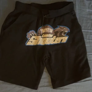 Trapstar shorts - Snygga svarta shorts från Trapstar med ett coolt 'London Shooters' tryck i beige och blått framtill. Perfekta för en avslappnad stil. Pris kan diskuteras 