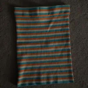 Säljer en tight, ribbad kjol med horisontella ränder i turkos, orange och vit. Kjolen är kort och har en stretchig passform som sitter snyggt på kroppen. Aldrig använd, mycket bra skick