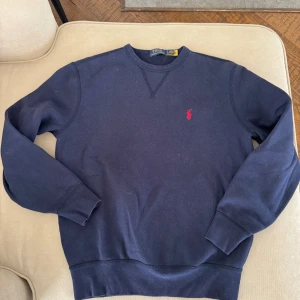 Mörkblå tröja från Polo Ralph Lauren - Säljer en stilren mörkblå tröja från Polo Ralph Lauren med det klassiska röda logotypbroderiet på bröstet. Tröjan har långa ärmar och rund halsringning, perfekt för en avslappnad look. Bomull. Bra skick. Pris går att diskutera. 