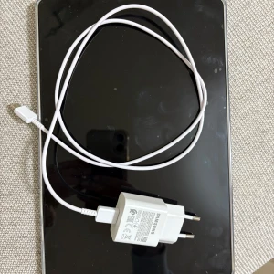 Samsung surfplatta med laddare och skal - Säljer en svart Samsung surfplatta med tillhörande vit laddare och genomskinligt skal. Plattan har en stilren design med rundade hörn och stor skärm. Perfekt för streaming, surf och appar. Laddare och skal ingår. ( har haft den i några månader bara) 