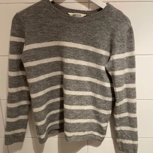 stickad tröja  - Mysig stickad tröja från H&M i grått med vita horisontella ränder. Tröjan har rund halsringning och långa ärmar, perfekt för kyligare dagar. Enkel och stilren design som passar till mycket.