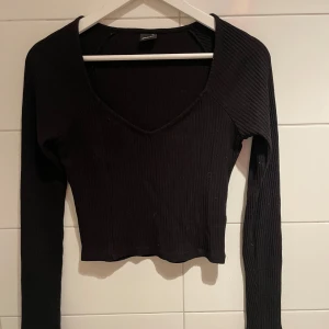 Tröja - Säljer en svart ribbad långärmad topp från Gina Tricot. Toppen har v-ringning och är croppad i modellen, vilket ger en trendig och stilren look. Perfekt att matcha med både jeans och kjol.